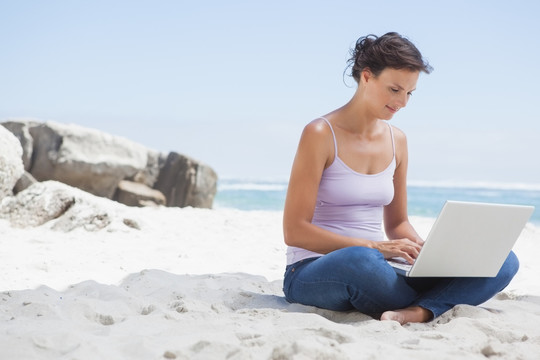 盘腿坐在沙滩上用电脑的女人