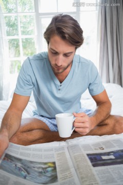 英俊男子坐在床上喝咖啡看书