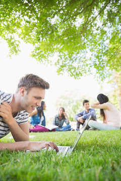 趴在草坪上使用电脑的男学生
