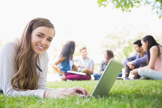 趴在草坪上使用电脑的女学生