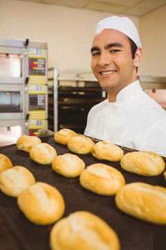 微笑的男面包师拿着一盘新鲜面包