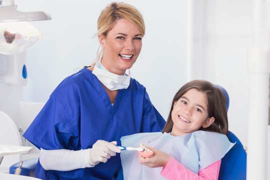 微笑的女牙医在教导女孩刷牙