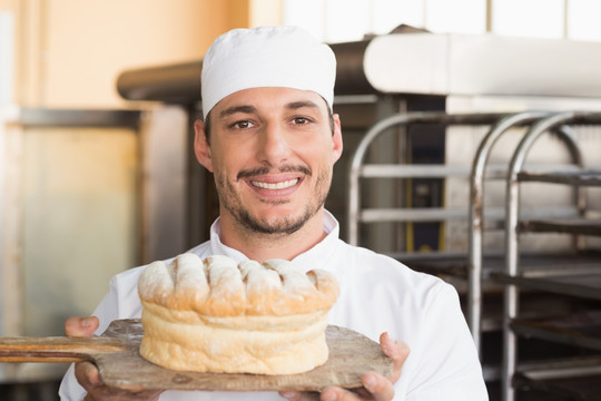 微笑的男面包师拿着一个面包