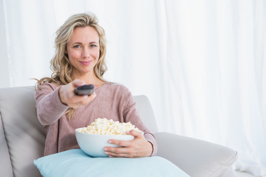 女人坐在沙发上看电视吃爆米花
