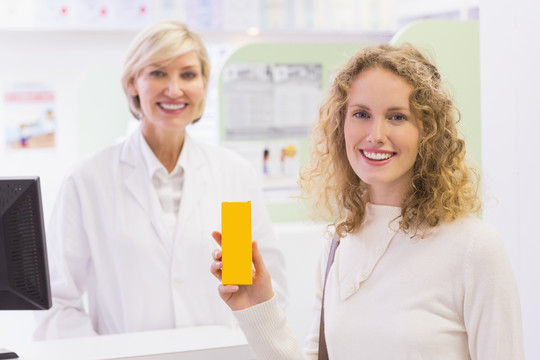 微笑的女顾客在药房里拿着一盒药