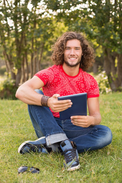 坐在公园草坪上用平板电脑的男人