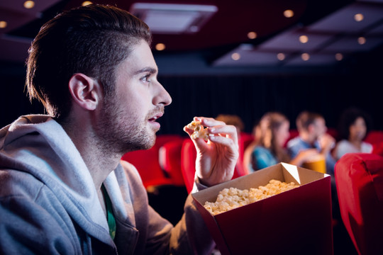 在电影院看电影吃爆米花的男人