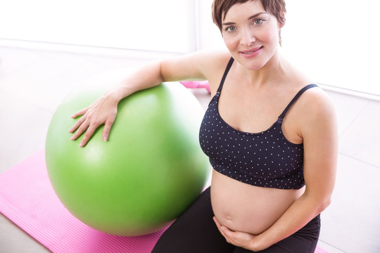 跪在瑜伽垫上单手托着肚子的孕妇
