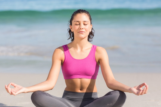 盘腿坐在沙滩上练瑜伽的女人