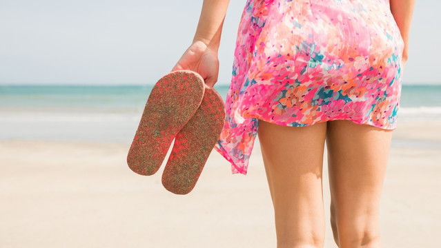 拿着拖鞋站在沙滩上的女人
