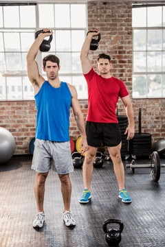 在健身房里举壶铃的两个男人
