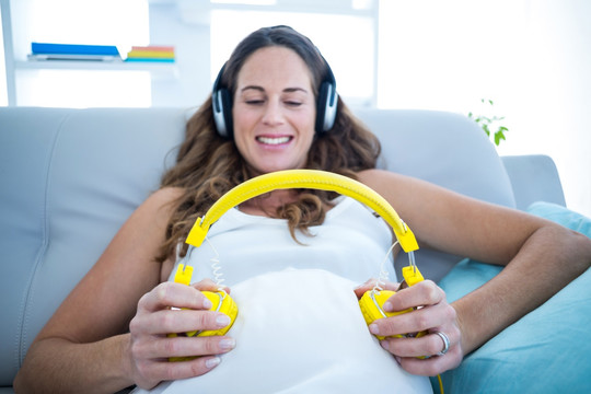 肚子上戴着耳机给宝宝听歌的孕妇