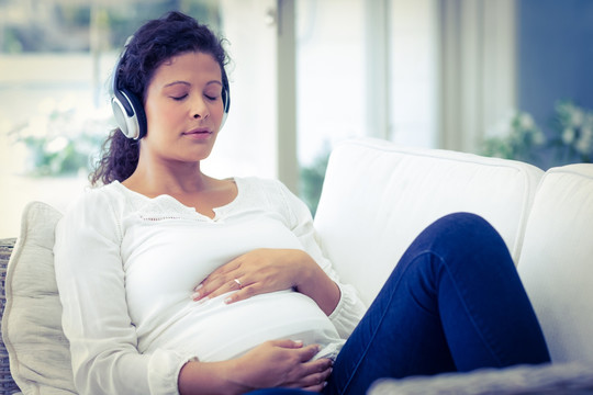 戴着耳机坐在沙发上的孕妇