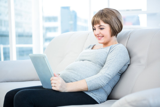 坐在沙发上使用平板电脑的孕妇