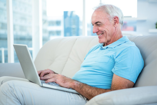 坐在沙发上使用笔记本电脑的老人