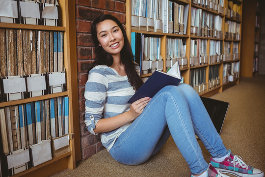 微笑的学生坐在图书馆地板上看书
