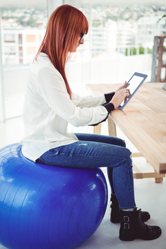 坐在健身球上使用平板电脑的女人