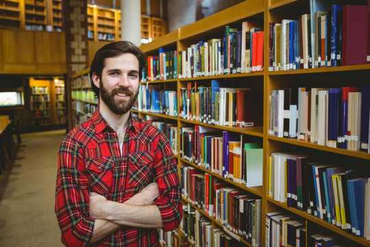 抱着双臂站在图书馆里的男大学生