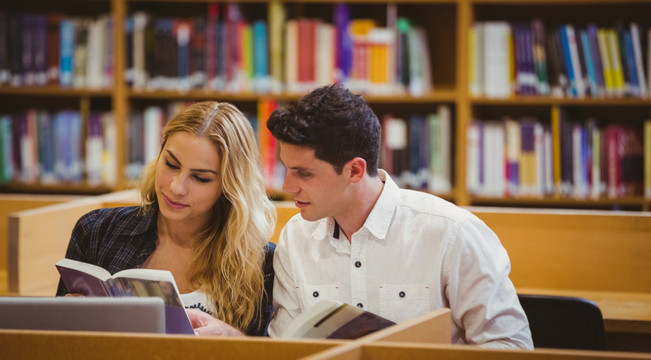 两名大学生坐在图书馆桌子前看书