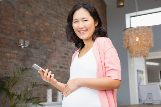 微笑的孕妇在家里拿着智能手机