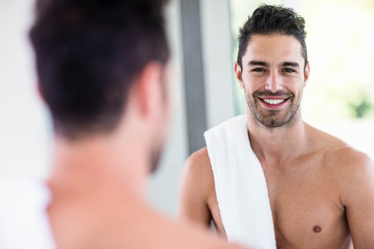 英俊的赤膊男子看着浴室里的镜子