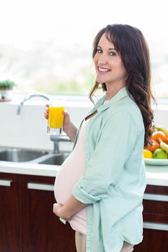 在厨房里拿着橙汁的孕妇