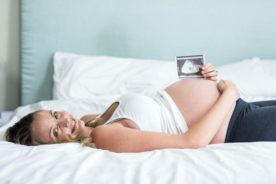 躺在床上的孕妇拿着一张超声照片