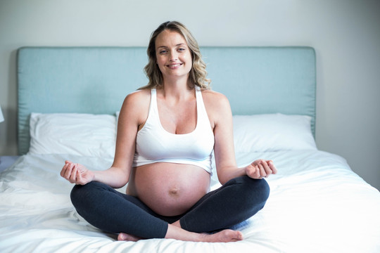 坐在床上练瑜伽的孕妇