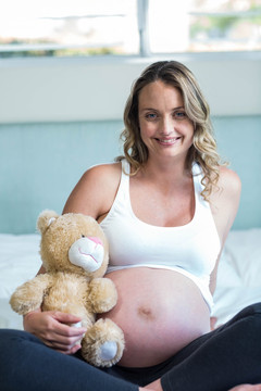 抱着泰迪熊坐在床上的孕妇