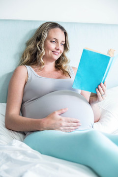 怀孕的女人躺在她的床上看书