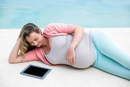 躺在泳池边的用平板电脑的孕妇