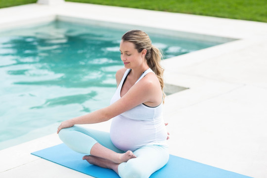 孕妇在游泳池边的垫子上做瑜伽