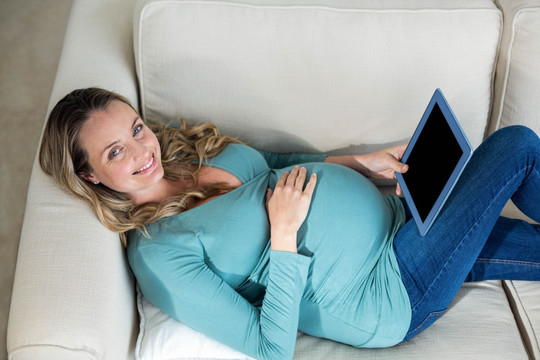 躺在沙发上使用平板电脑的孕妇