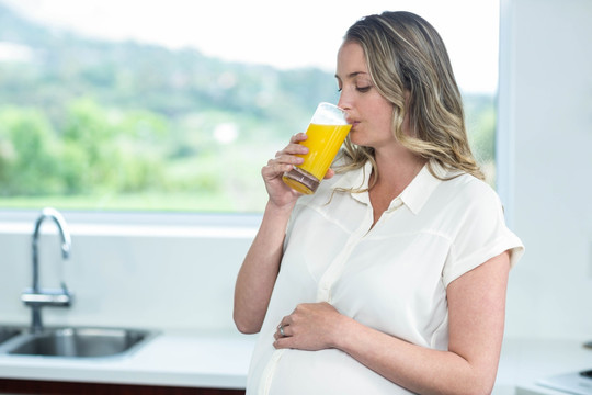 孕妇在厨房里喝一杯橙汁