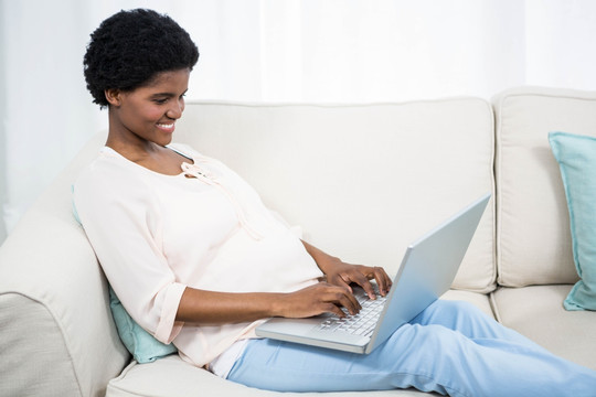 坐在沙发上使用笔记本电脑的孕妇