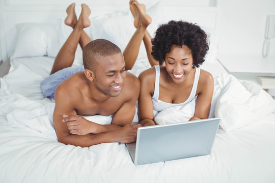 微笑的夫妇在床上使用笔记本电脑