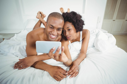 在床上使用手机自拍的夫妇
