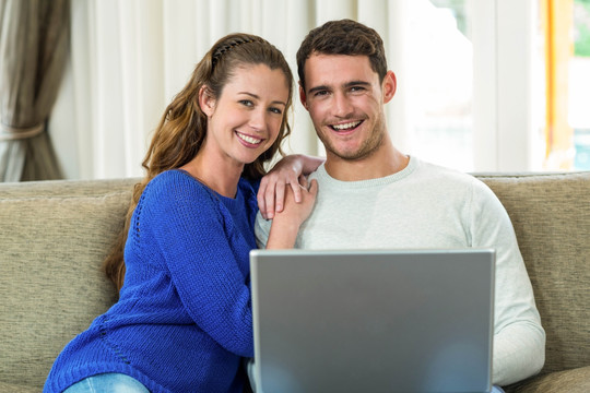 一对年轻夫妇坐在沙发上用电脑