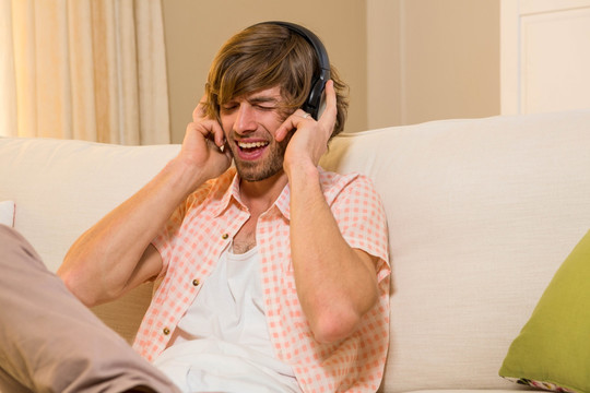 坐在沙发上戴着耳机听音乐的男人