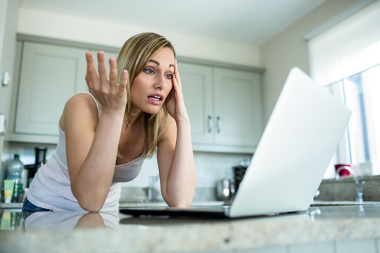 惊讶的女人在家里用笔记本电脑