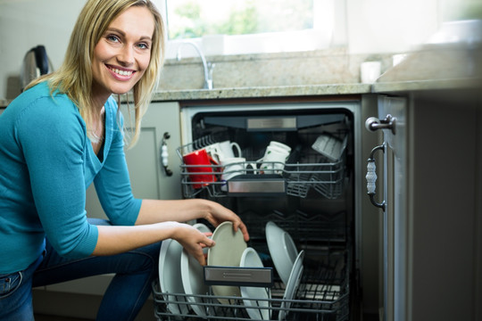 微笑的女人从洗碗机里拿一个盘子