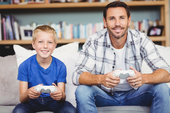 坐在沙发上玩游戏机的父亲和儿子