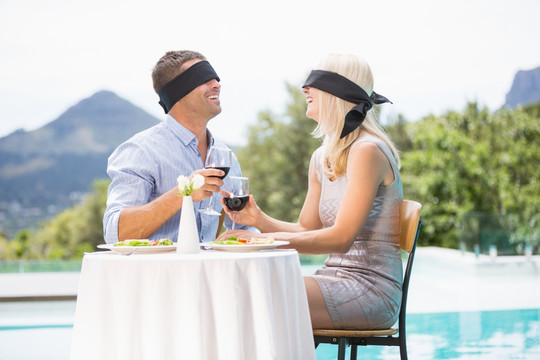 蒙着眼睛的夫妇在游泳池旁喝红酒