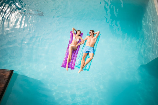 在泳池里躺在充气垫上的一对夫妇