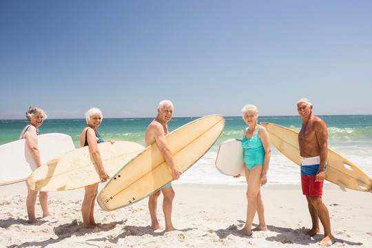 拿着冲浪板站在沙滩上的老人们