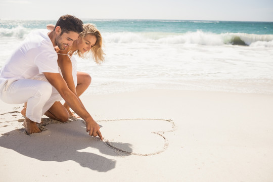 在沙滩上画爱心的夫妇