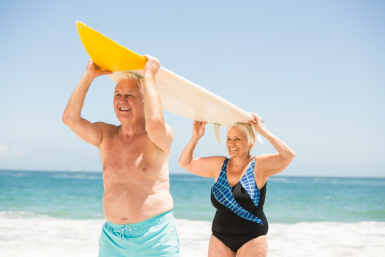 在海边举着冲浪板的老夫妇