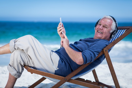 躺在沙滩椅上听歌用手机的男人