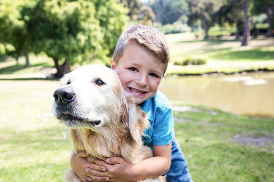 微笑的男孩抱着宠物狗在公园里