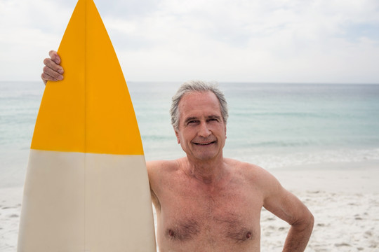 拿着冲浪板站在沙滩的老人